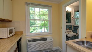 A compact kitchen with a microwave, a window, a sink, and a radiator. - Cape Cod Harbor House Inn (Hyannis)