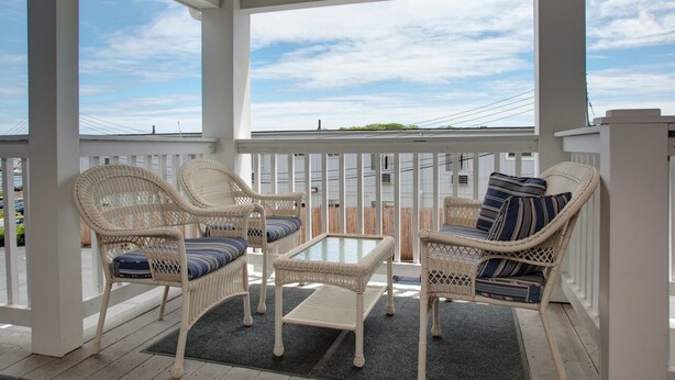 A covered outdoor seating area with wicker furniture and a glass-top table. - Cape Cod Harbor House Inn (Hyannis)