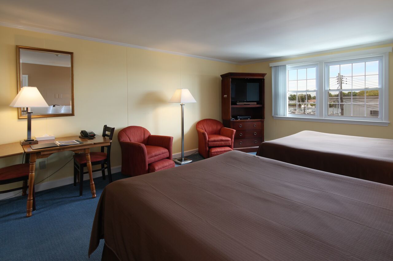 A hotel room with two beds, a desk with a lamp, a chair, a television, and a window with a view of the outside.