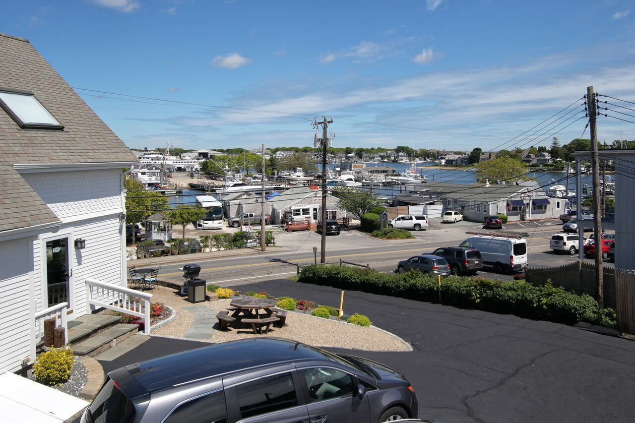 A marina with boats docked, a parking area with cars, and a building with a porch.