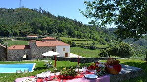 Une table à manger installée à l’extérieur, offrant une vue sur un paysage verdoyant et luxuriant, avec un bâtiment en arrière-plan.