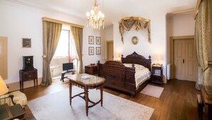 Une chambre à coucher avec un lit en bois, un lustre, un bureau et une fenêtre avec des rideaux.