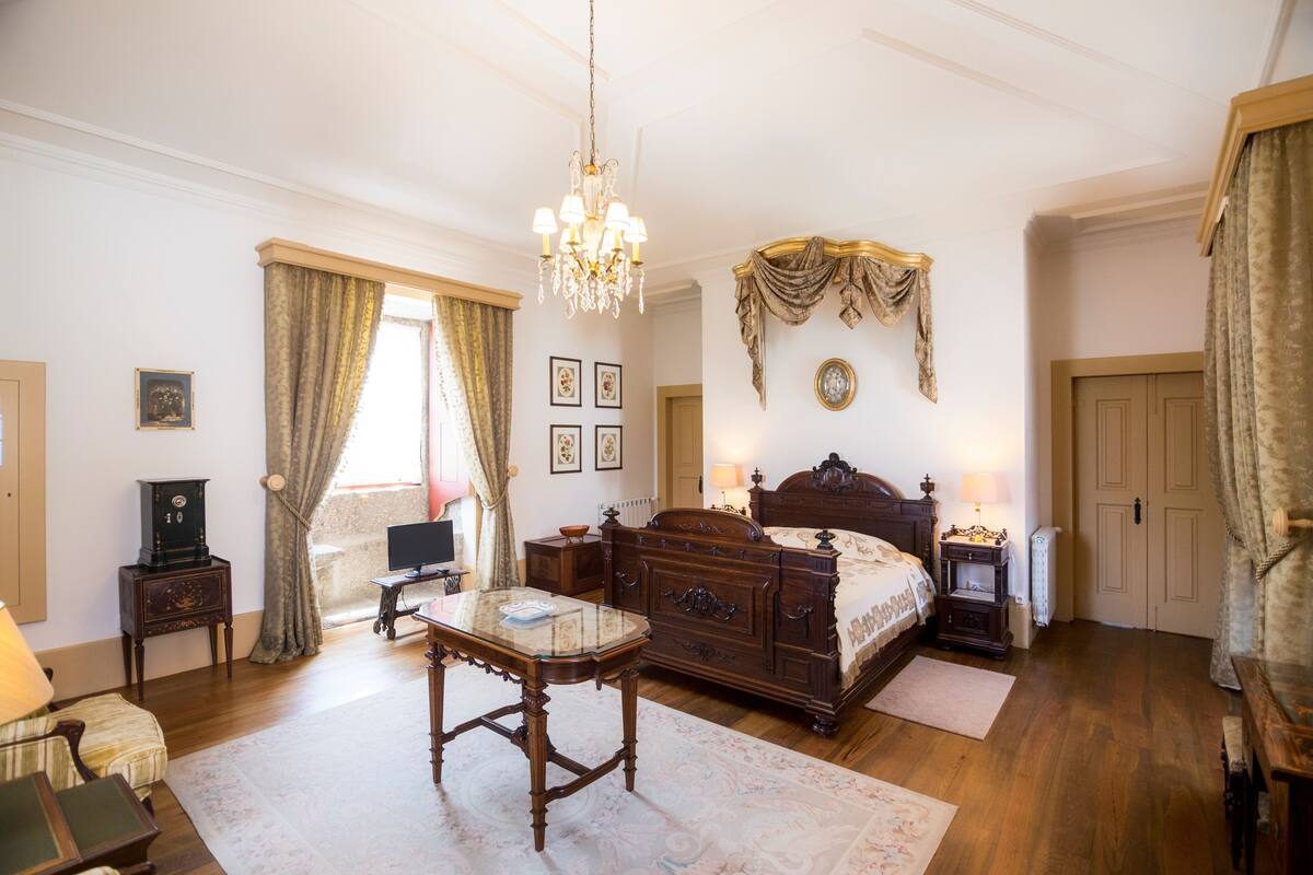 Een slaapkamer met een houten bed, een kroonluchter, een bureau en een raam met gordijnen.