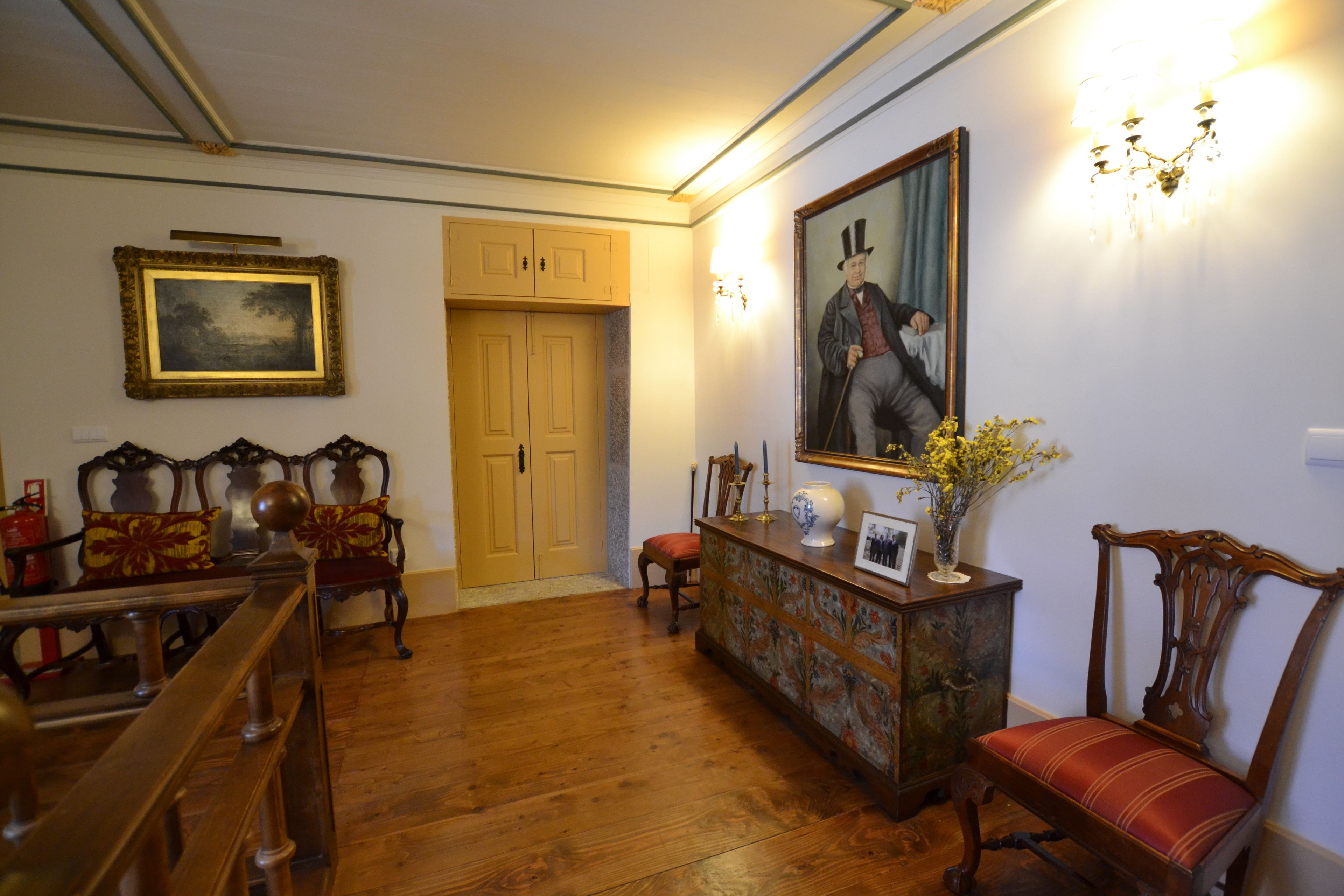A room with wooden flooring, a wooden bench, a wooden chair, a wooden table, and a wooden cabinet with a mirror and a vase with flowers.