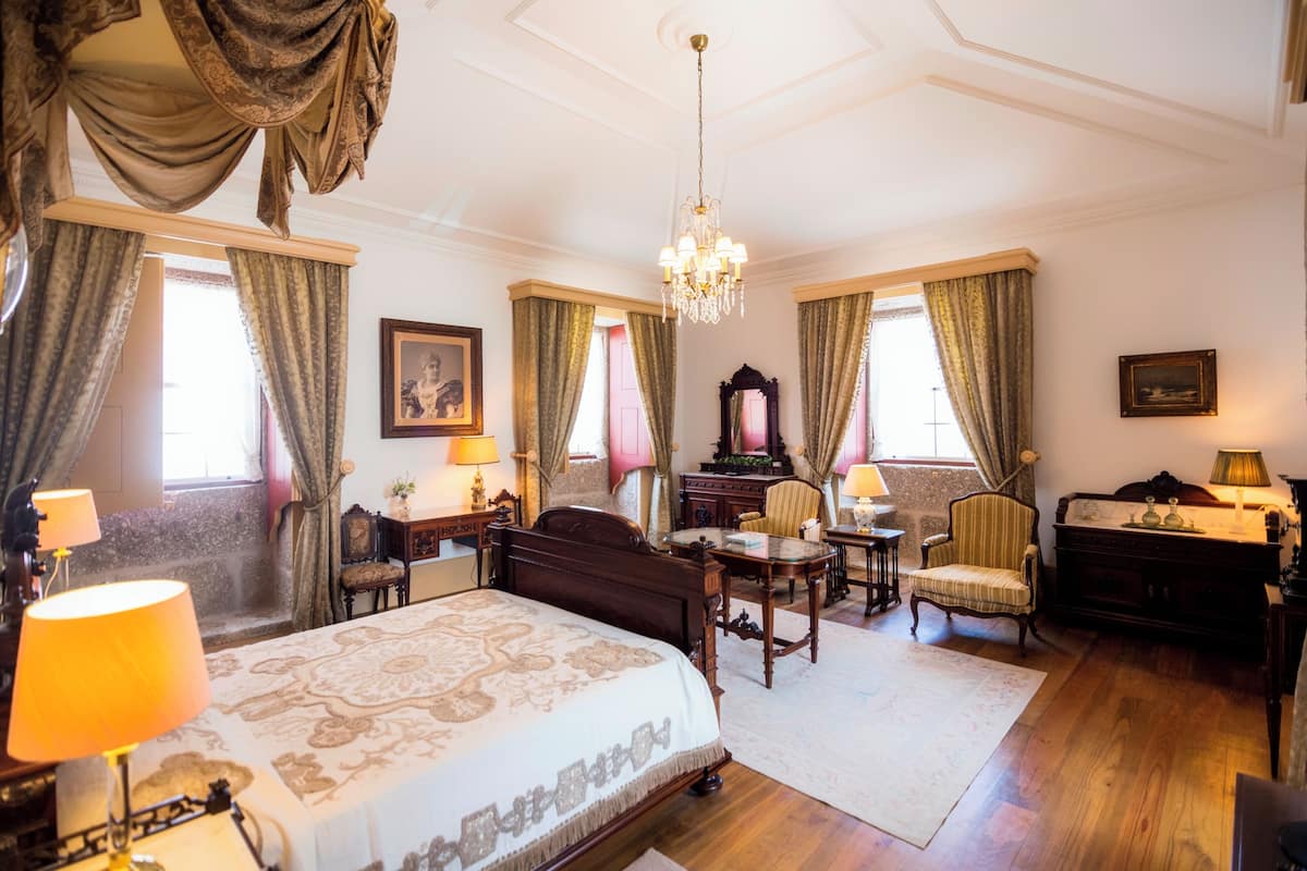 Een klassieke kamer met een groot bed, een bureau, een stoel en een dressoir.
