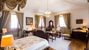 A classic hotel room with a large bed, a desk, a chair, and a chandelier.