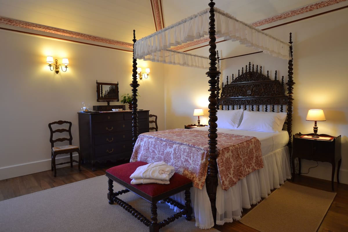 Een hemelbed, een nachtkastje met een lamp, een stoel en een dressoir met lades.
