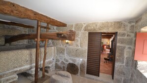 Un intérieur rustique avec des murs en pierre, un escalier en bois, un mur de pierre et une porte donnant sur une autre pièce.