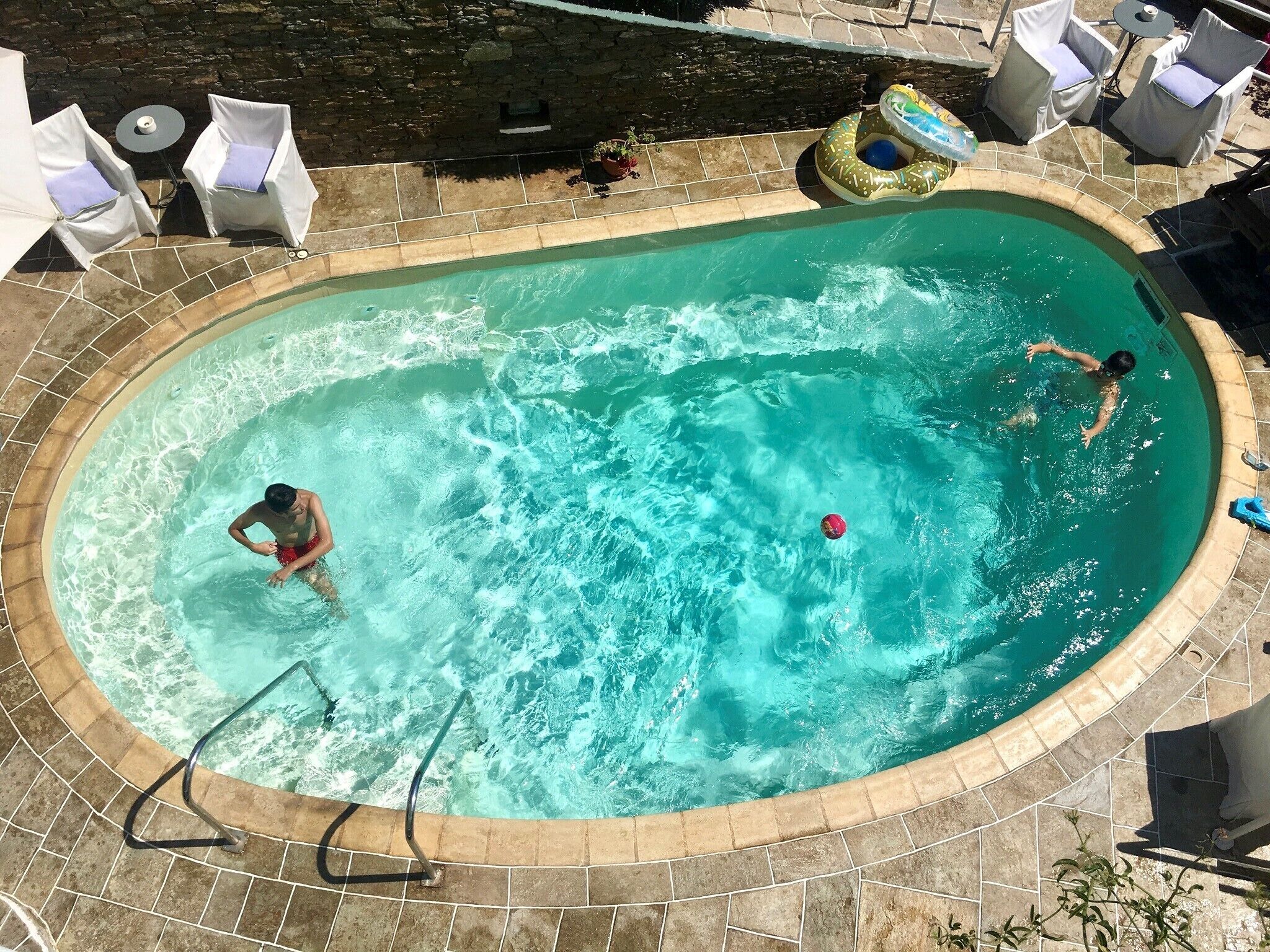 Une piscine extérieure bordée de pierres, avec des chaises longues et une petite table.