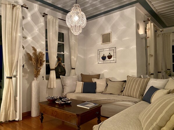 A cozy living room with a sofa, a wooden coffee table, and a hanging light fixture. - Niriedes Hotel (Sifnos)