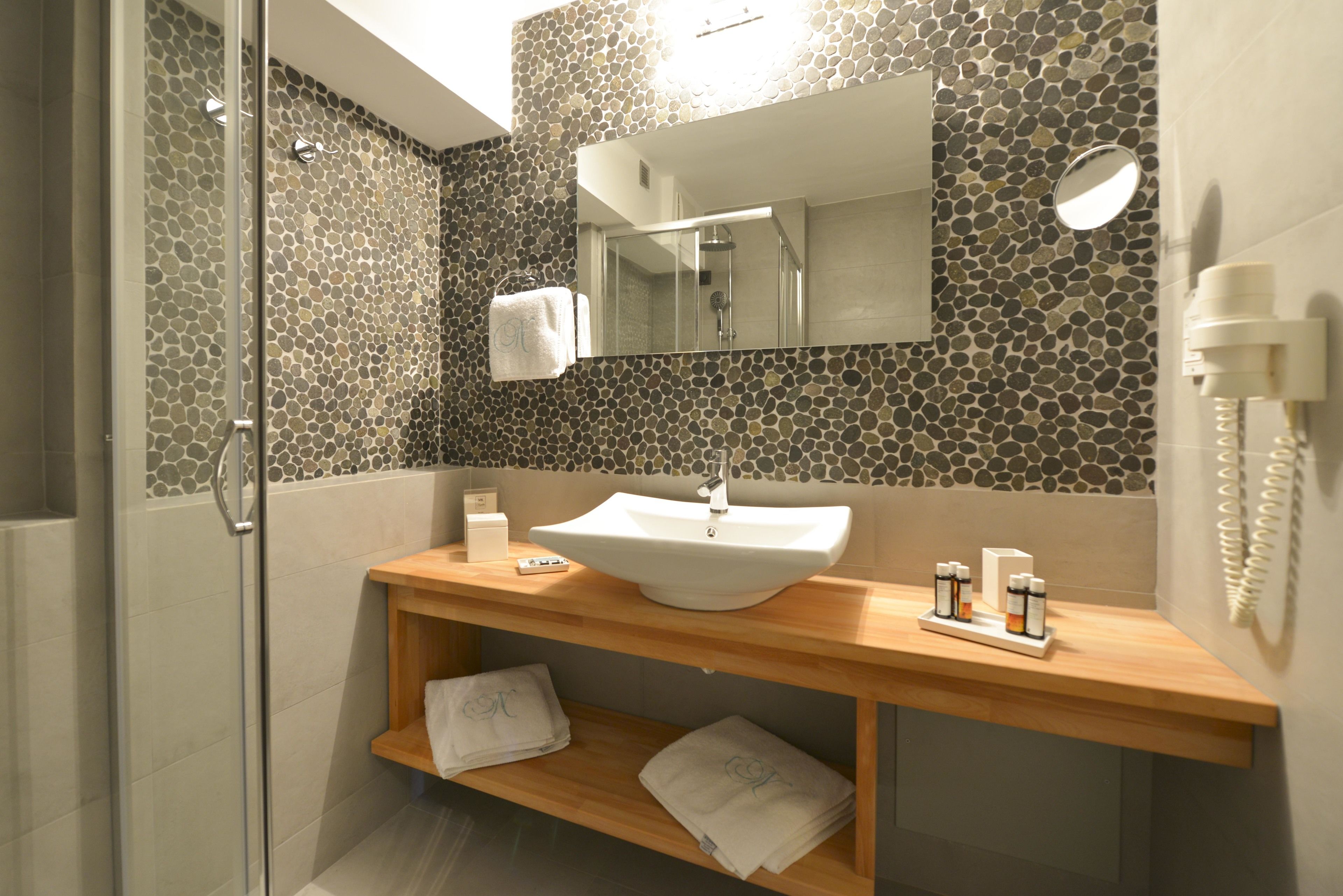 Une salle de bain moderne avec un mur décoré d’une mosaïque de pierre, un lavabo blanc et un meuble-vasque en bois.
