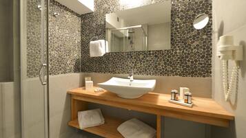 Une salle de bain moderne avec un mur décoré d’une mosaïque de pierre, un lavabo blanc et un meuble-vasque en bois.