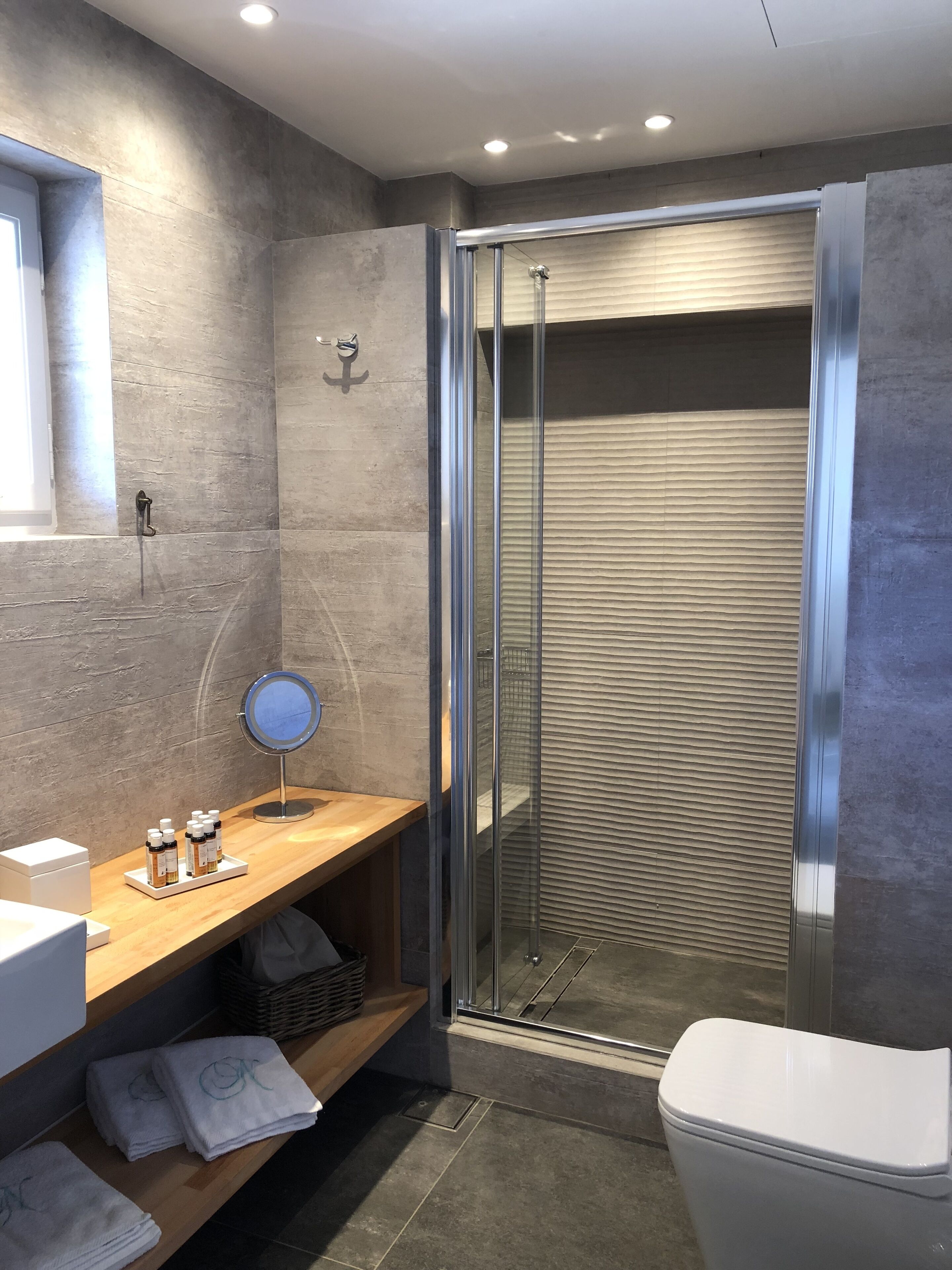 A modern bathroom with a glass shower enclosure, a wooden vanity with a mirror, and neatly folded towels.