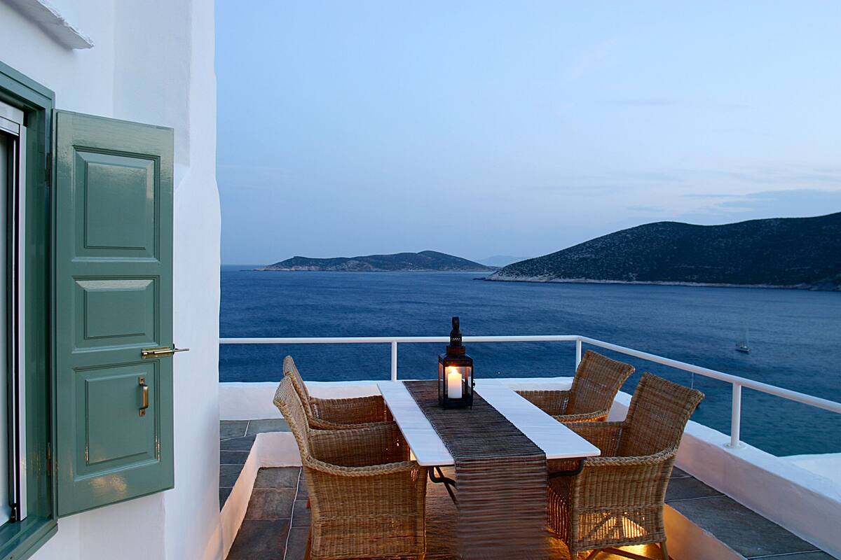 Ein Balkon mit Korbmöbeln und einem Tisch, mit Blick auf ein Gewässer und entfernte Landstriche.