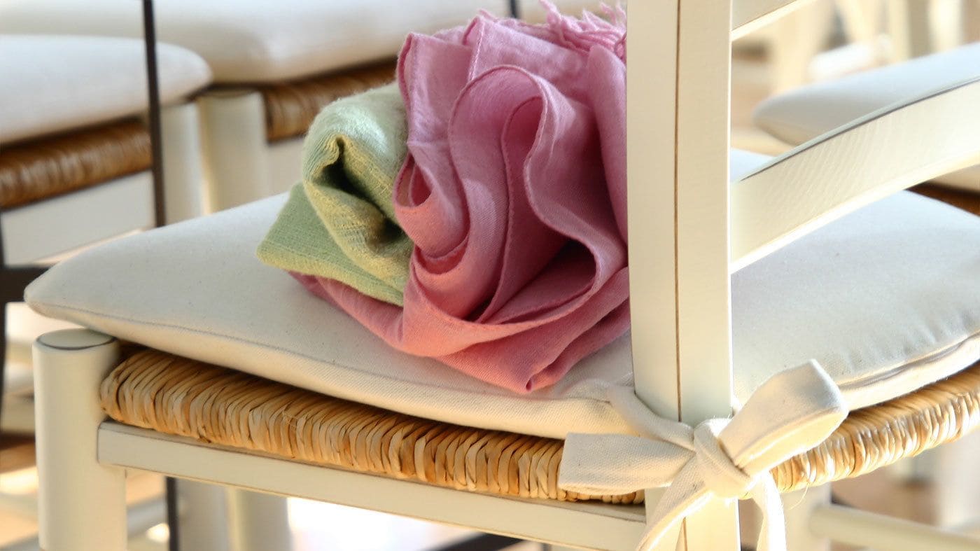 Una silla con asiento y respaldo trenzados, y un cojín de tela rosa y verde.