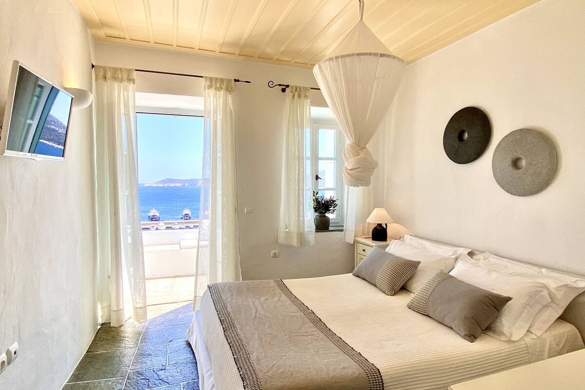 Ein Schlafzimmer mit Bett, Fernseher, Meerblick und einer Topfpflanze.
