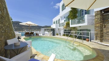 Uma área de piscina com espreguiçadeiras e guarda-sóis, uma parede de pedra e vista para as montanhas.