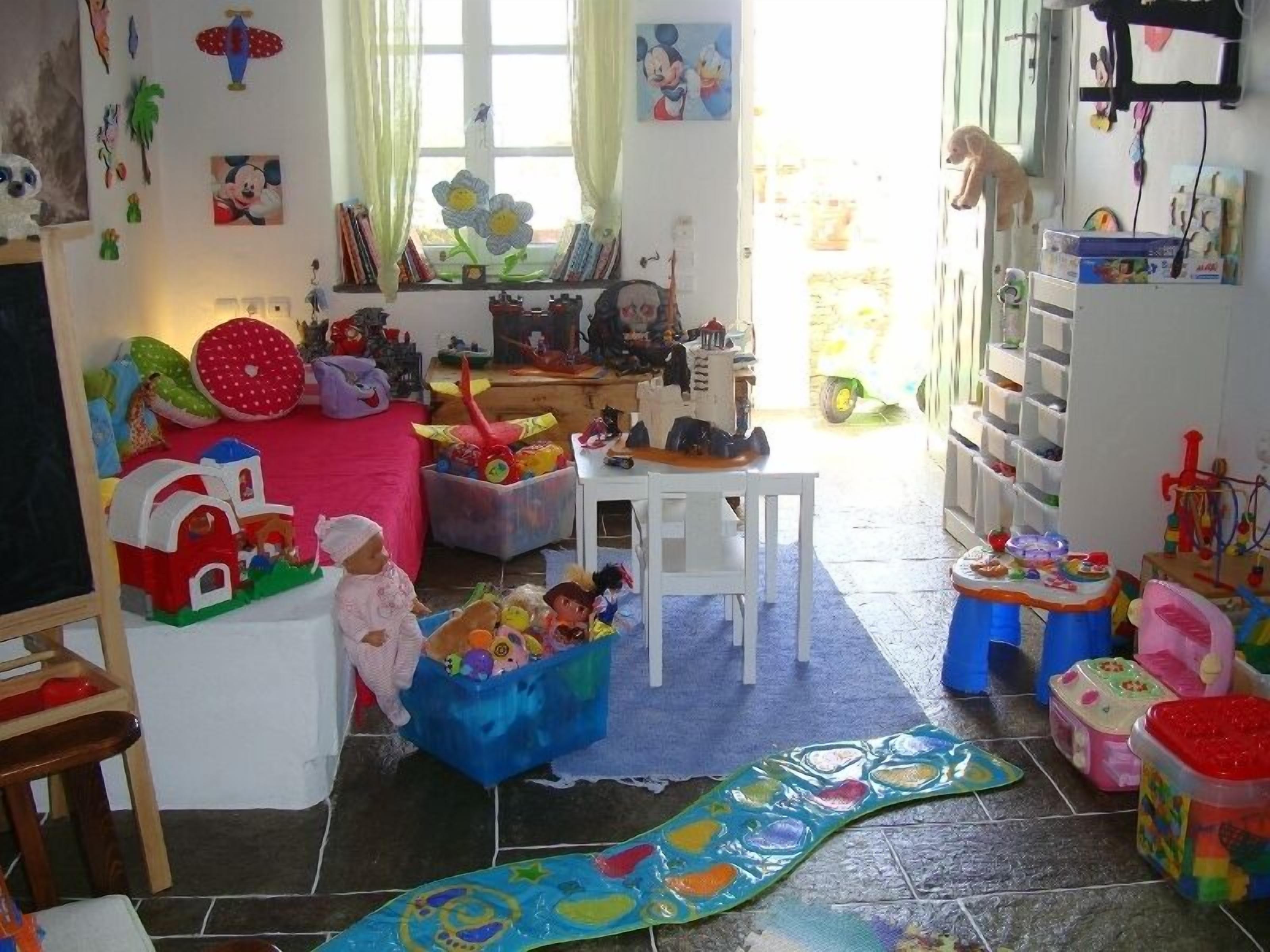 A child's playroom with toys, a play mat, and a window with curtains.