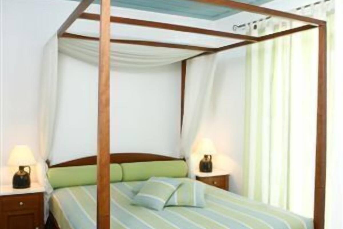 Ein Bett mit Baldachin, zwei Nachttische mit Lampen, eine grüne gepolsterte Bank und ein gefliester Boden.