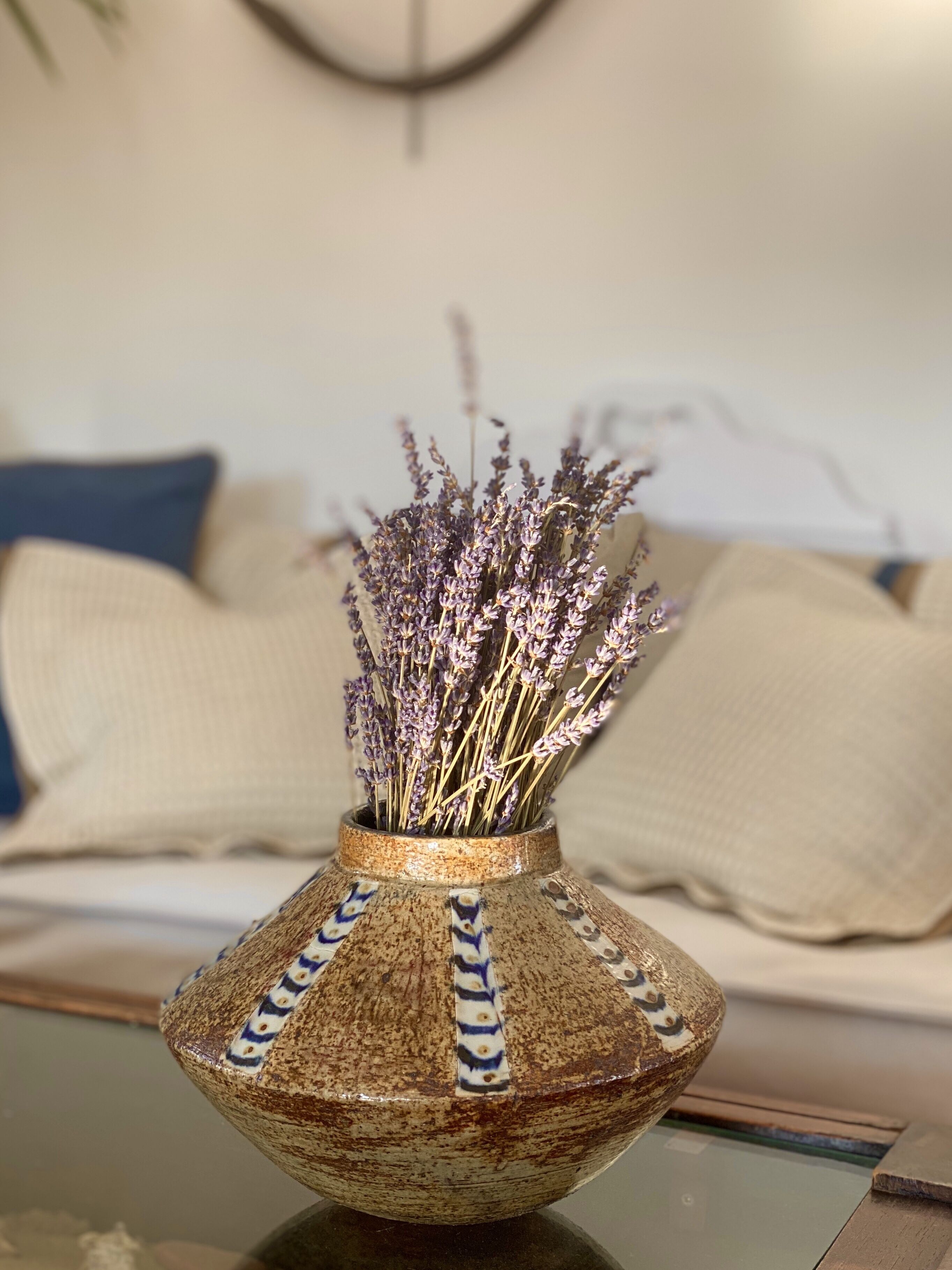 Een keramische vaas met een structuurpatroon, gevuld met gedroogde lavendelbloemen, op een glazen tafel.