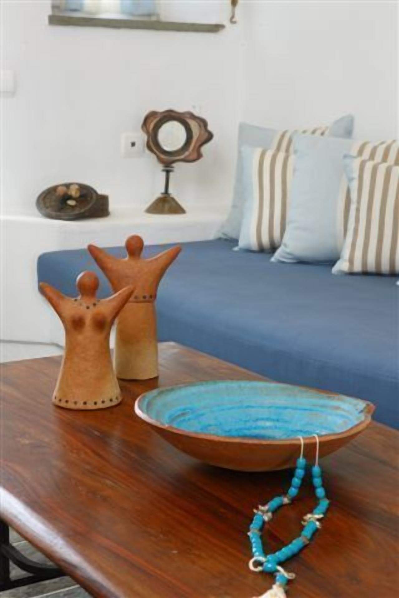Een houten tafel met een keramieken kom, een blauwe kralenketting en twee houten figuurtjes.