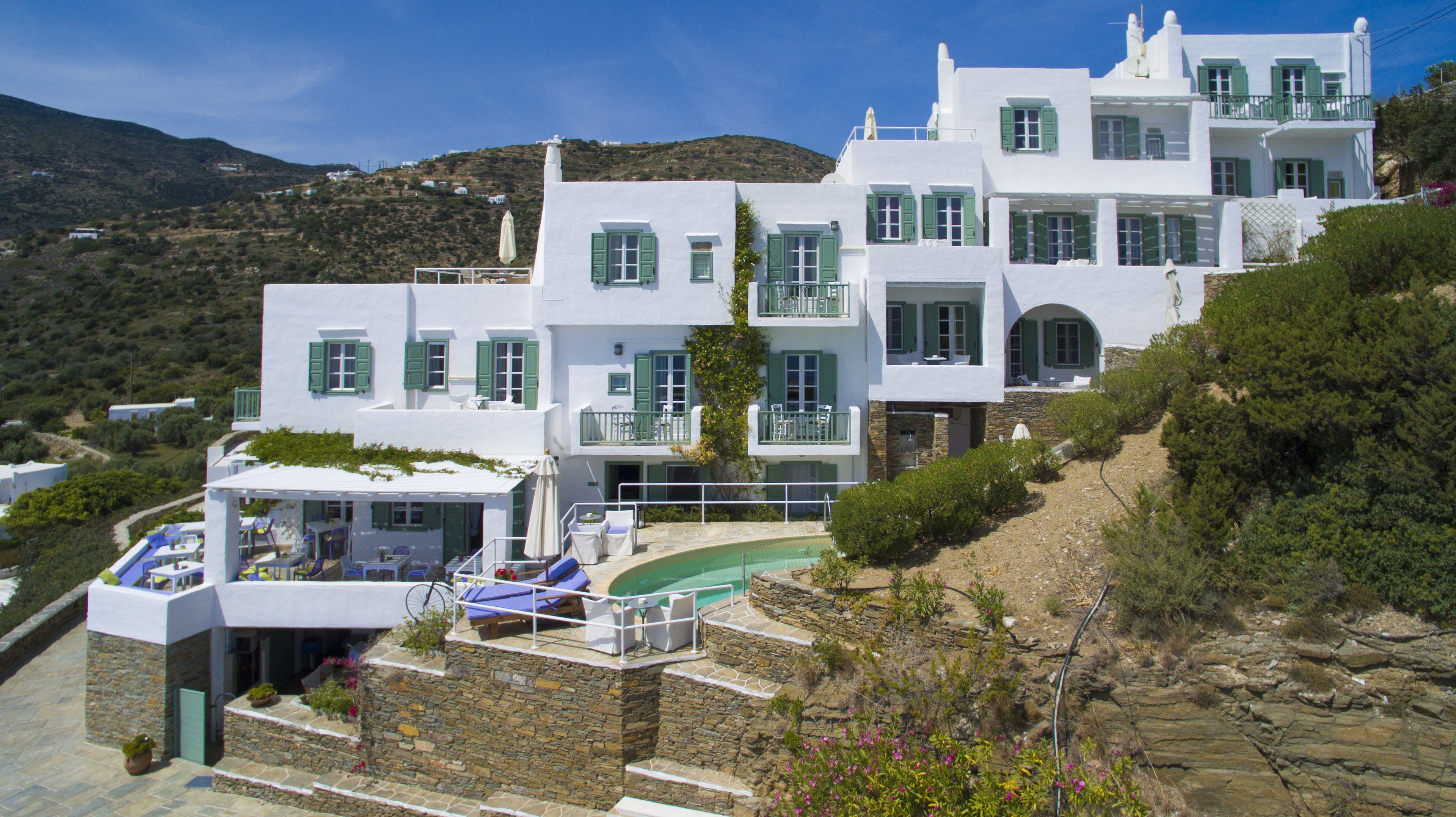 Un edificio blanco con contraventanas verdes, una piscina y montañas al fondo.
