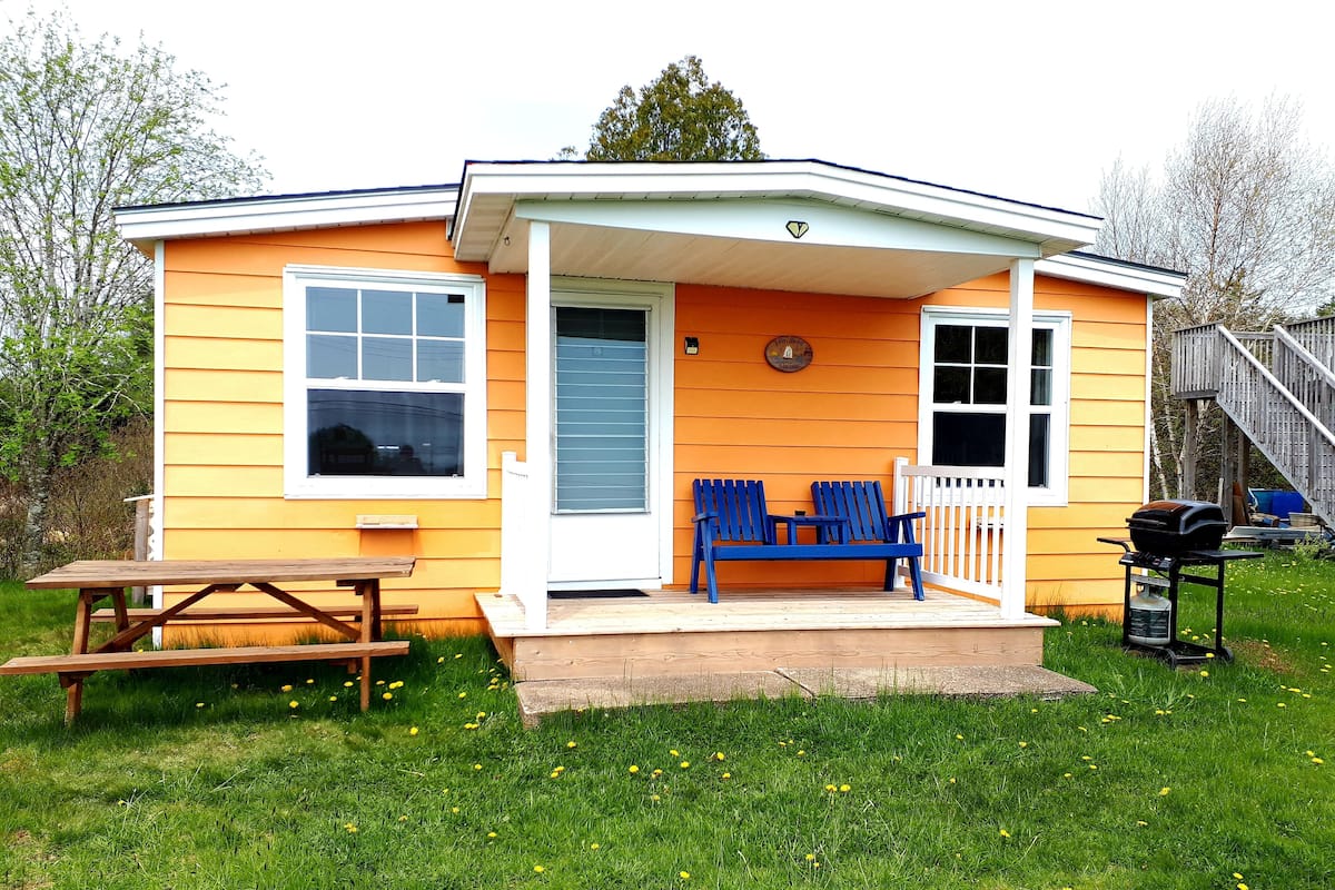 A yellow house with a porch, a picnic table, and a barbecue grill.