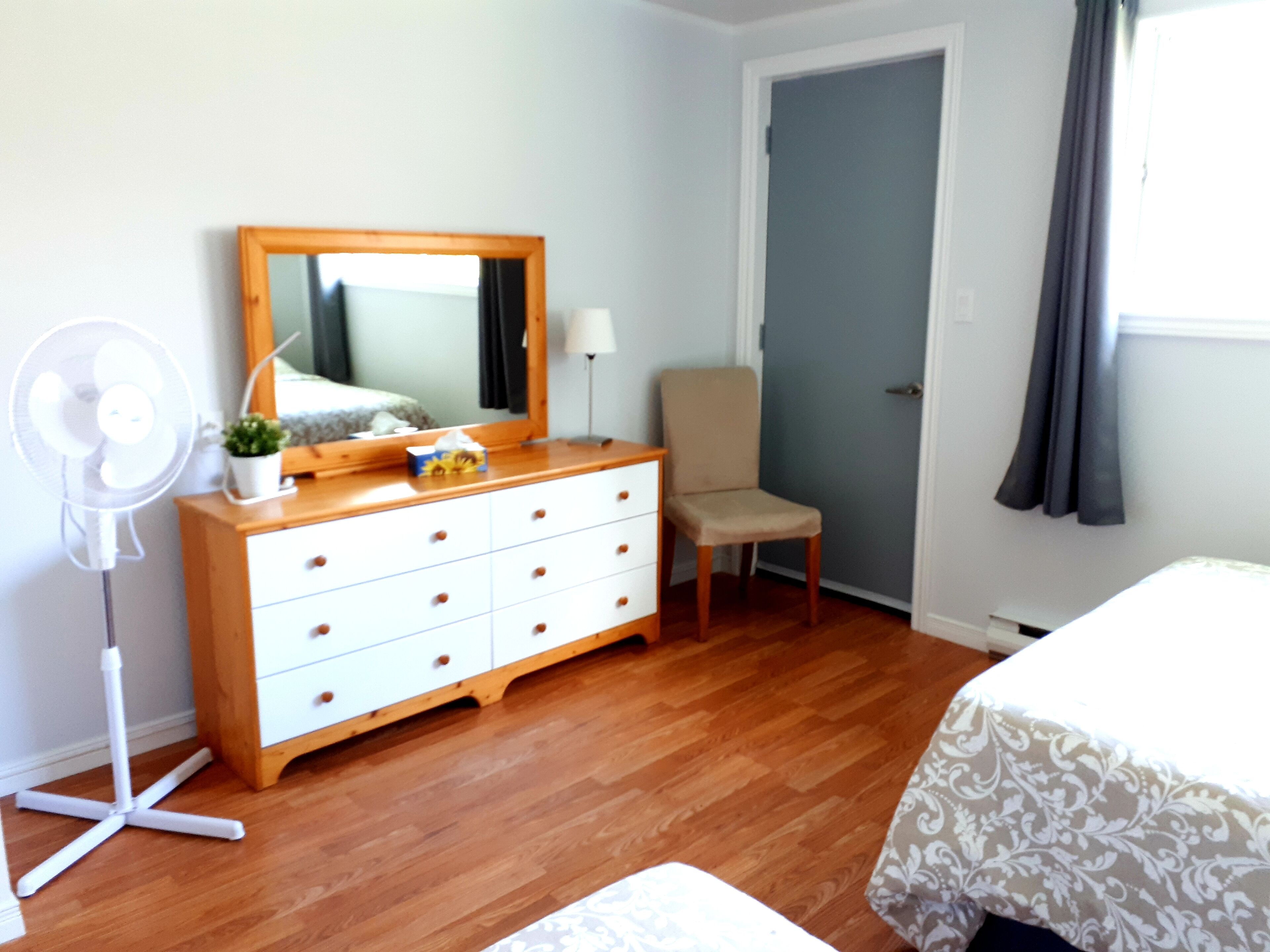 A bedroom with a wooden dresser, a chair, a bedside table, and a bed.
