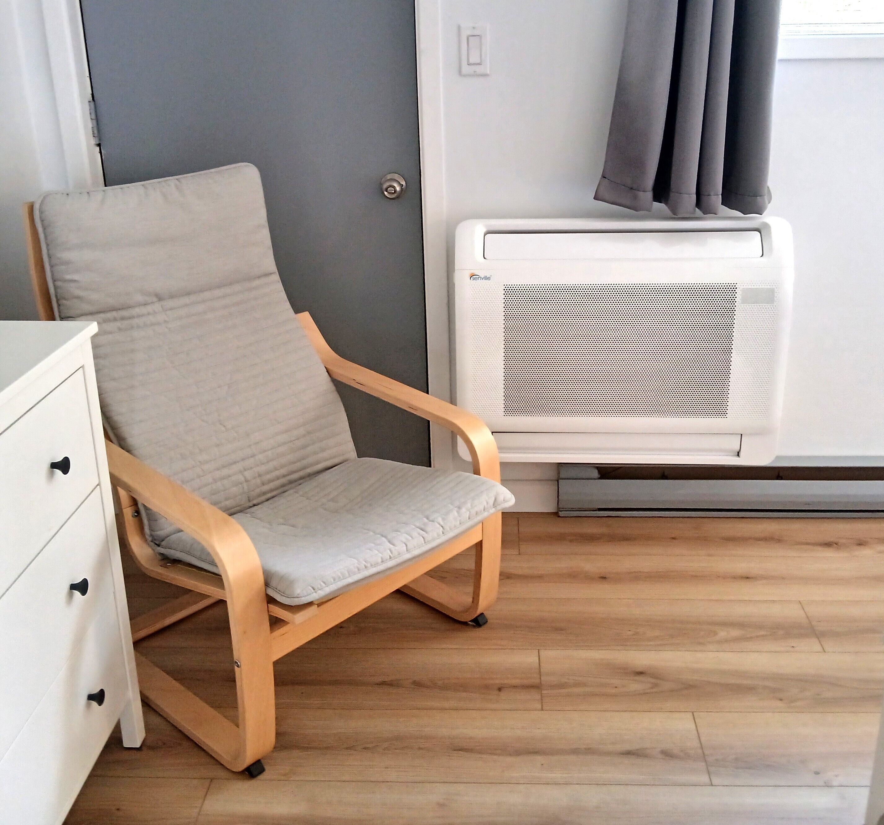 A room with a wooden chair, a white dresser, and a white air conditioning unit.