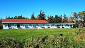 Un motel de dos pisos con techo rojo, fachada azul y varias sillas y mesas azules en el césped delantero.