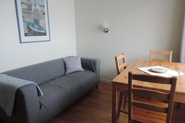 A room with a grey sofa, a wooden dining table with chairs, and a framed picture on the wall. - Atlantic View Motel and Cottages (Lunenburg)