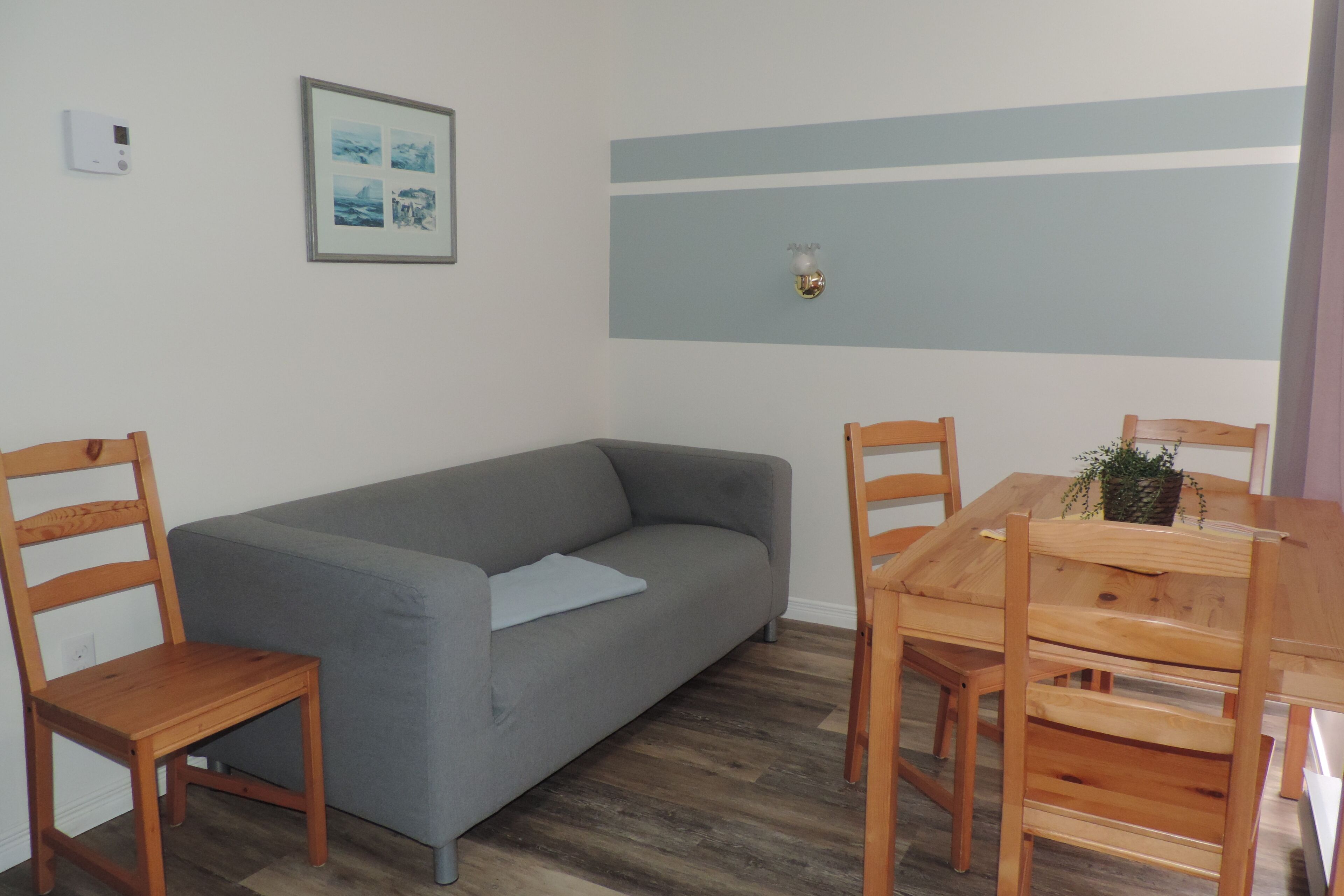 Una habitación con un sofá gris, sillas de madera, una mesa de madera y un cuadro en la pared.