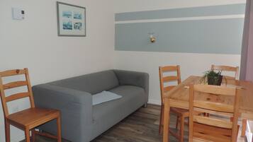 Una habitación con un sofá gris, sillas de madera, una mesa de madera y un cuadro en la pared.