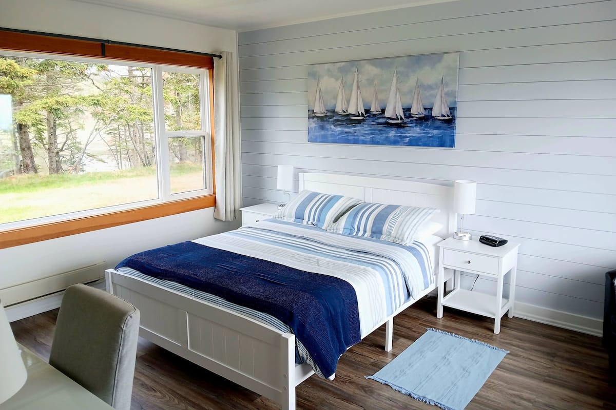 A bedroom with a bed, a nightstand, a lamp, and a painting of sailboats on the wall.