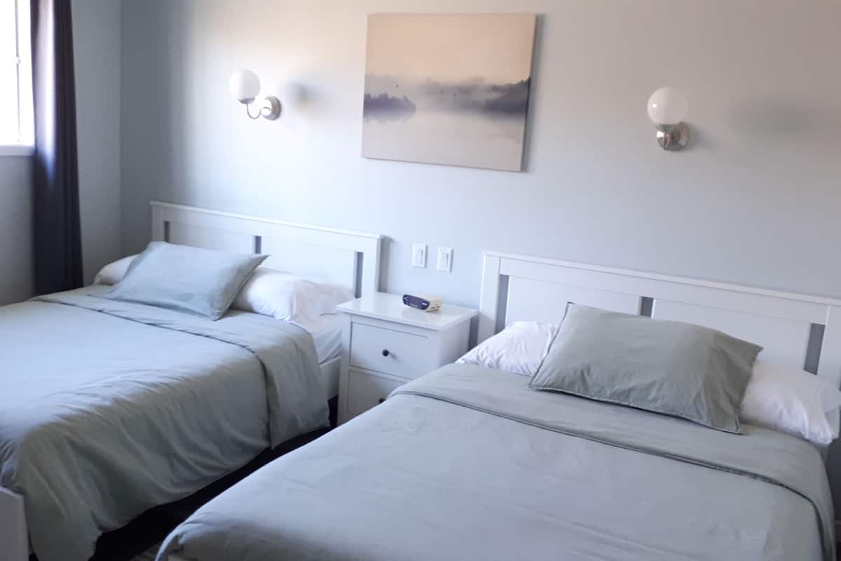 A hotel room with two single beds, a bedside table with a radio, and a painting on the wall.