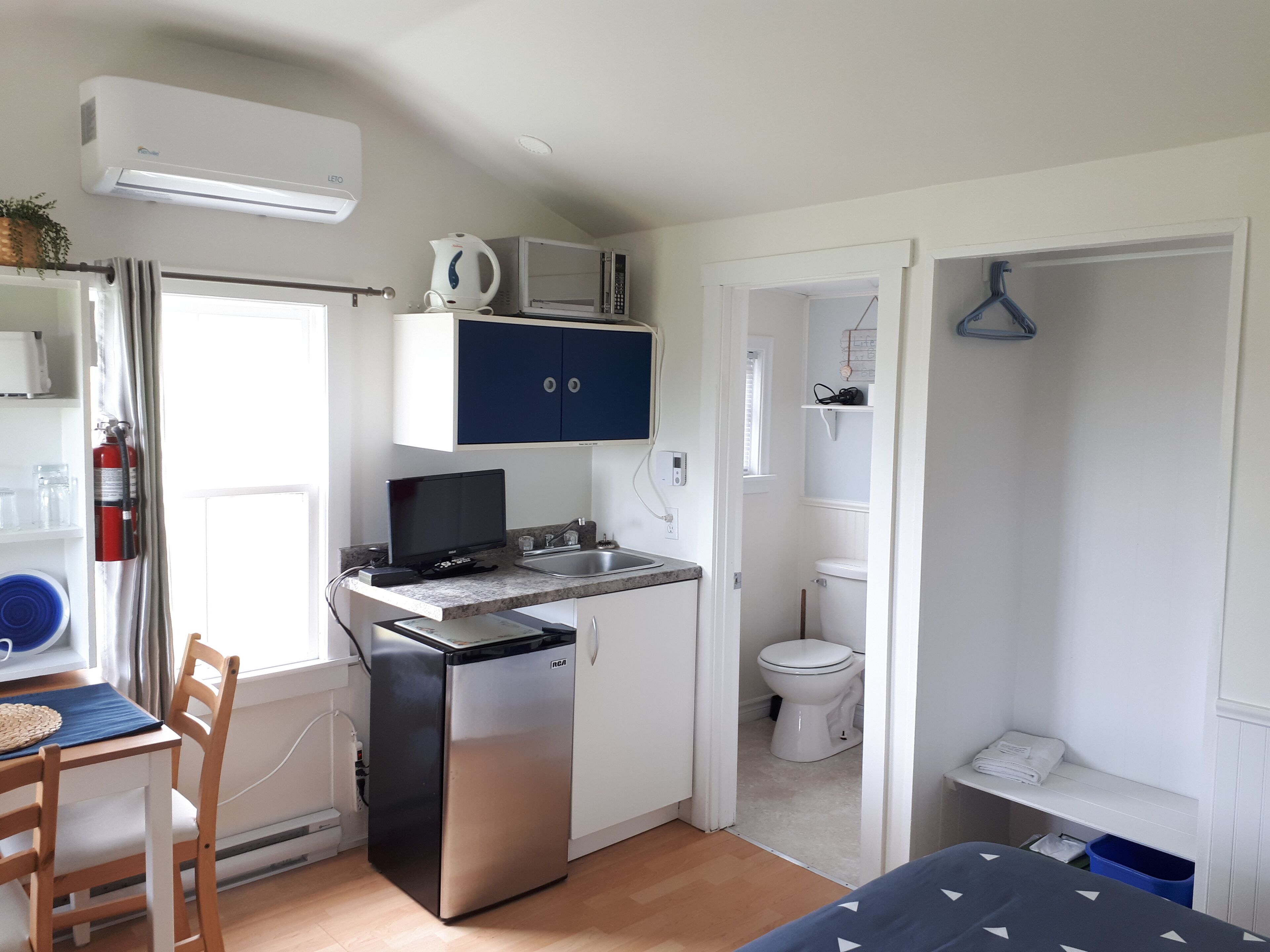 A compact kitchen with a refrigerator, microwave, and sink. There is a dining area with a table and chairs. A small bathroom with a toilet and shower is visible.