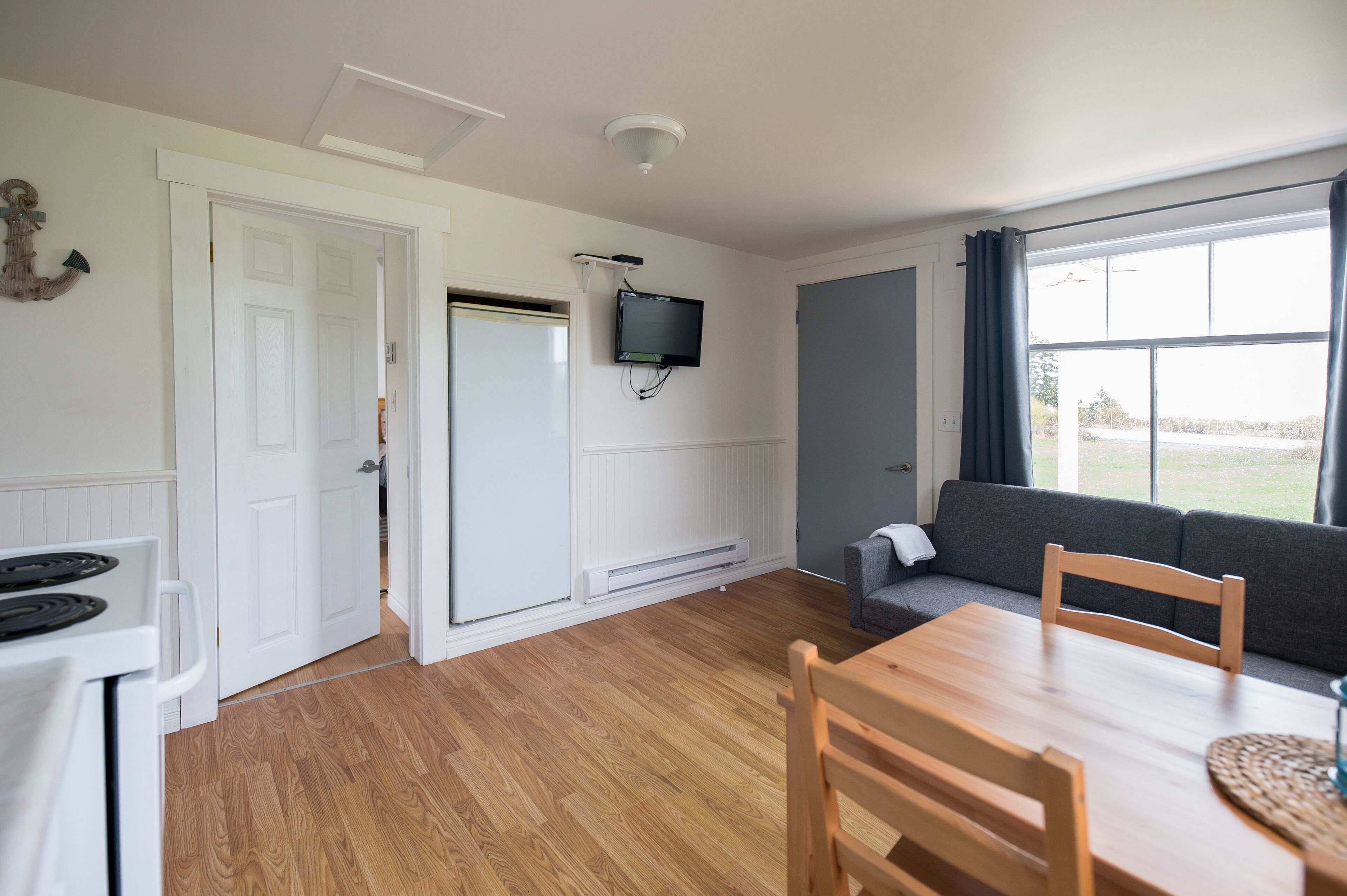 A room with a wooden floor, white walls, a gray sofa, a wooden table, and a TV mounted on the wall.