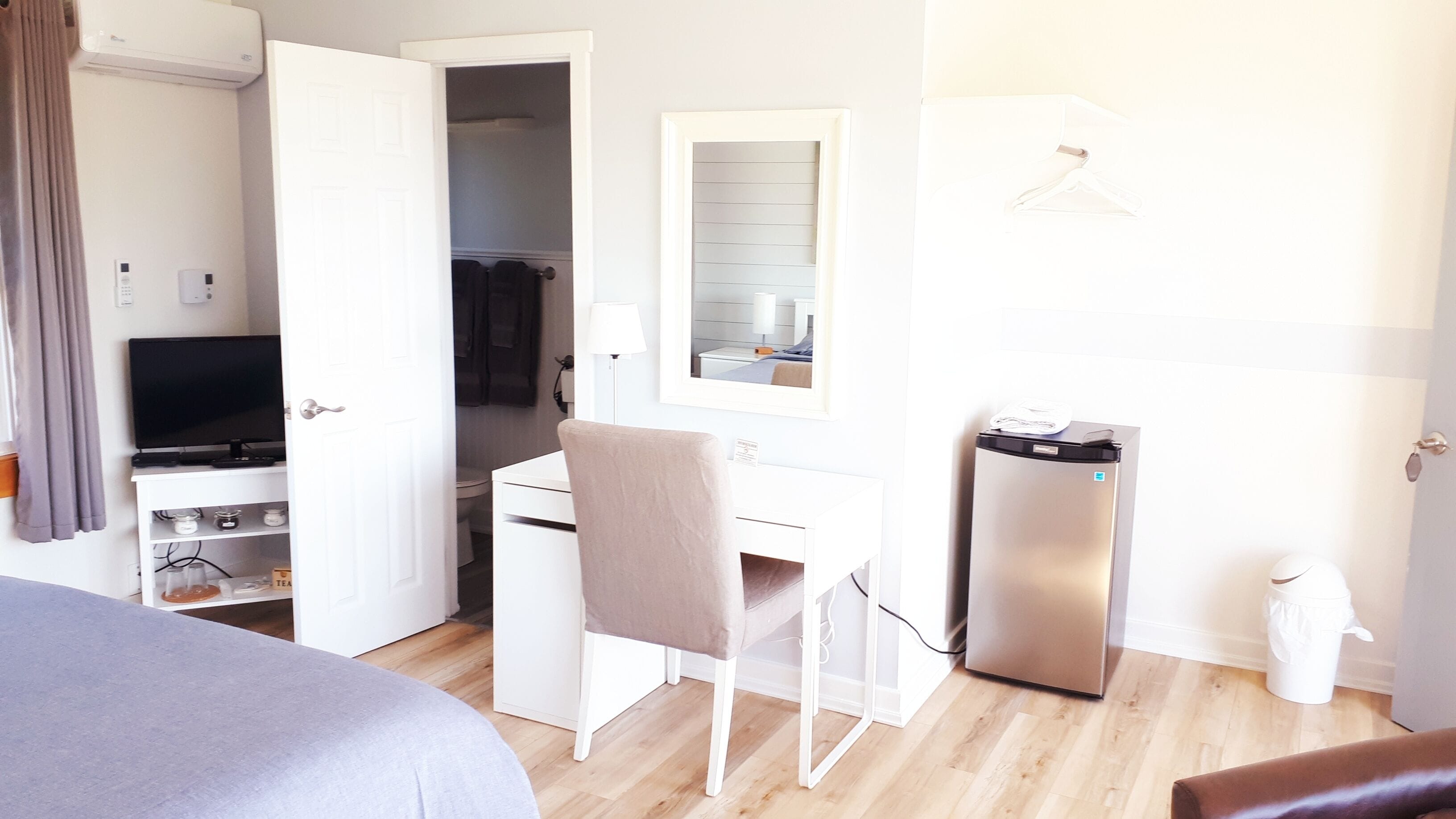 A hotel room with a bed, a desk with a chair, a television, a wardrobe, and a small refrigerator.