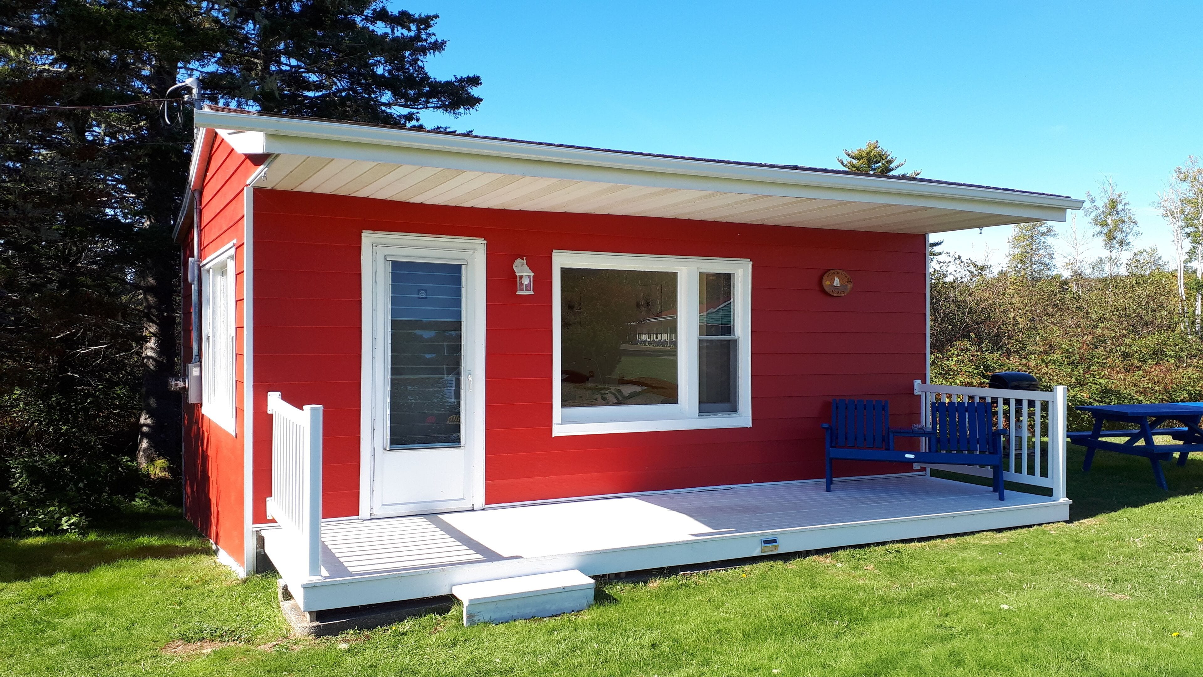 A small, red building with a white door and windows, a porch, and a blue bench.