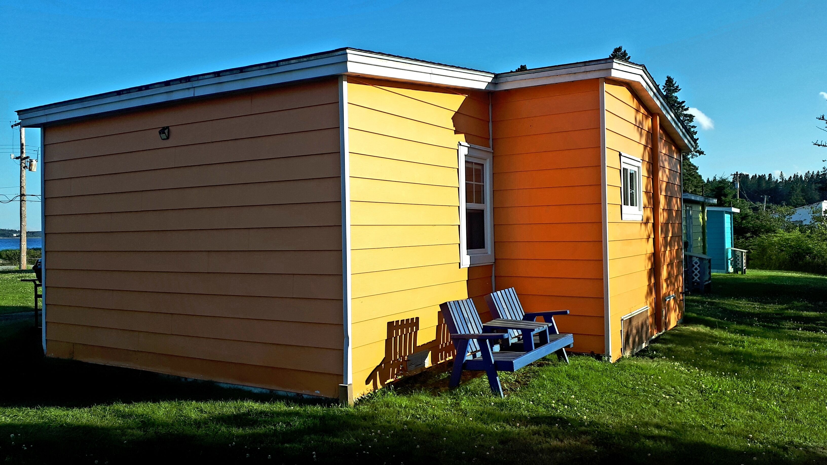 Un bâtiment jaune à deux étages, doté d’un petit porche et d’une chaise bleue.