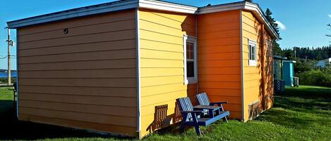 A two-story yellow building with a small porch and a blue chair.