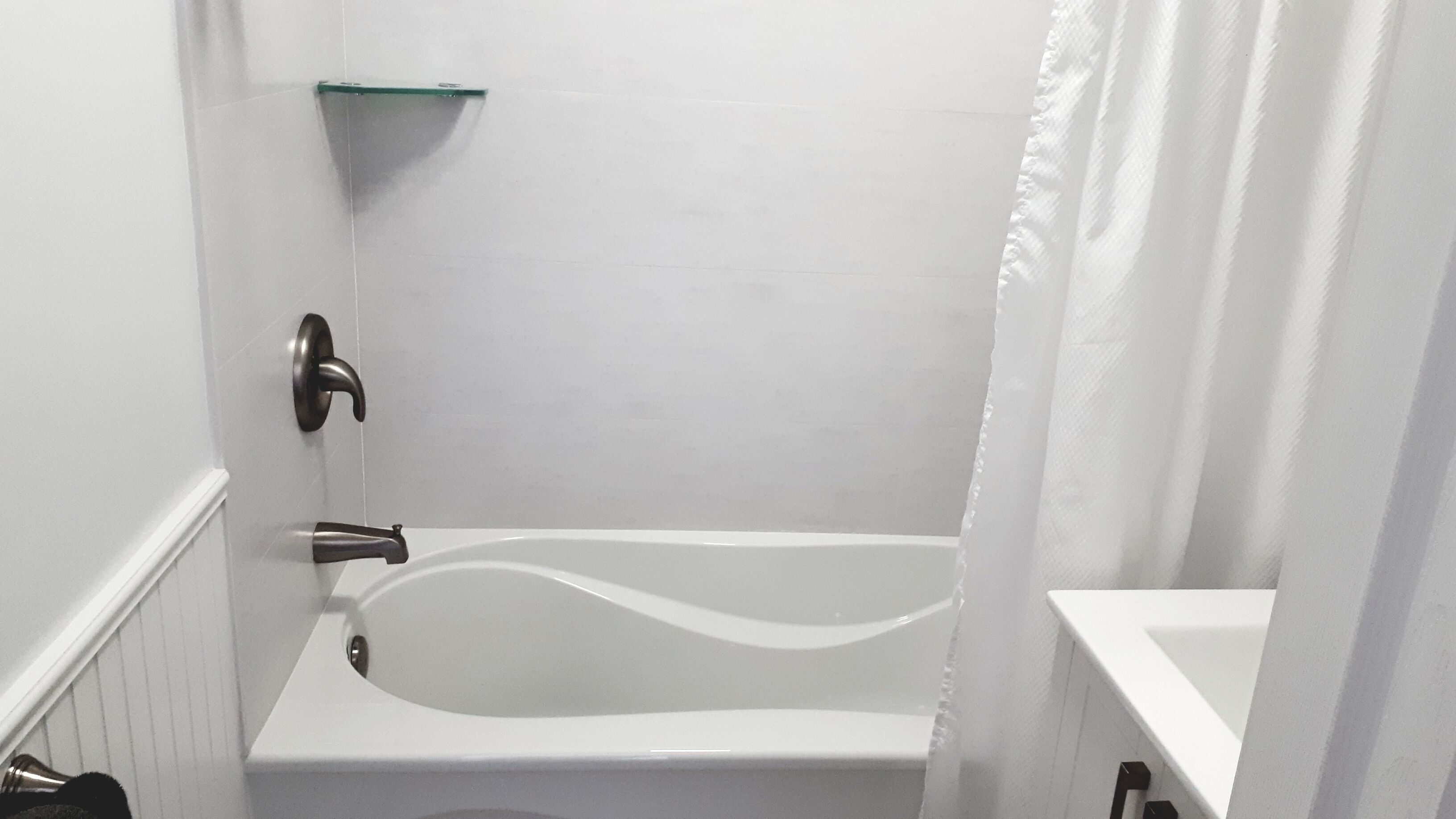 Un baño con una bañera blanca, un estante de vidrio y una cortina de ducha.