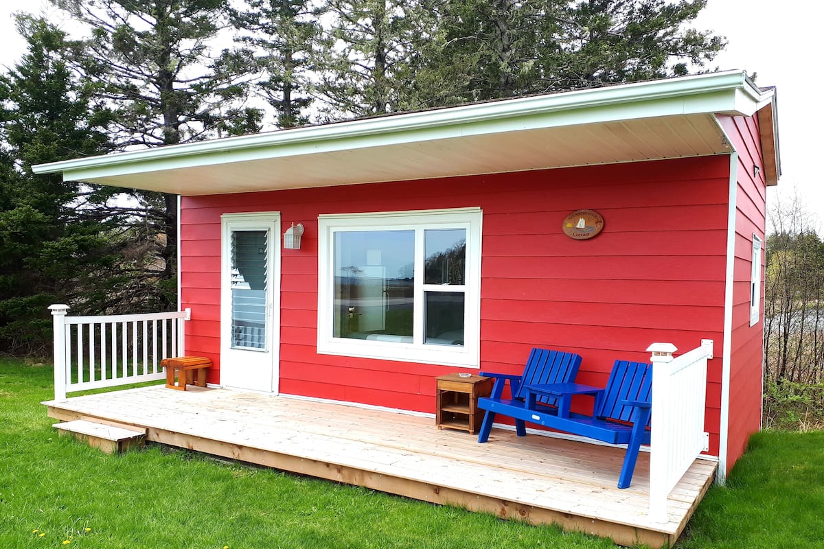 A red cottage with a white porch, two blue Adirondack chairs, and a small wooden table.