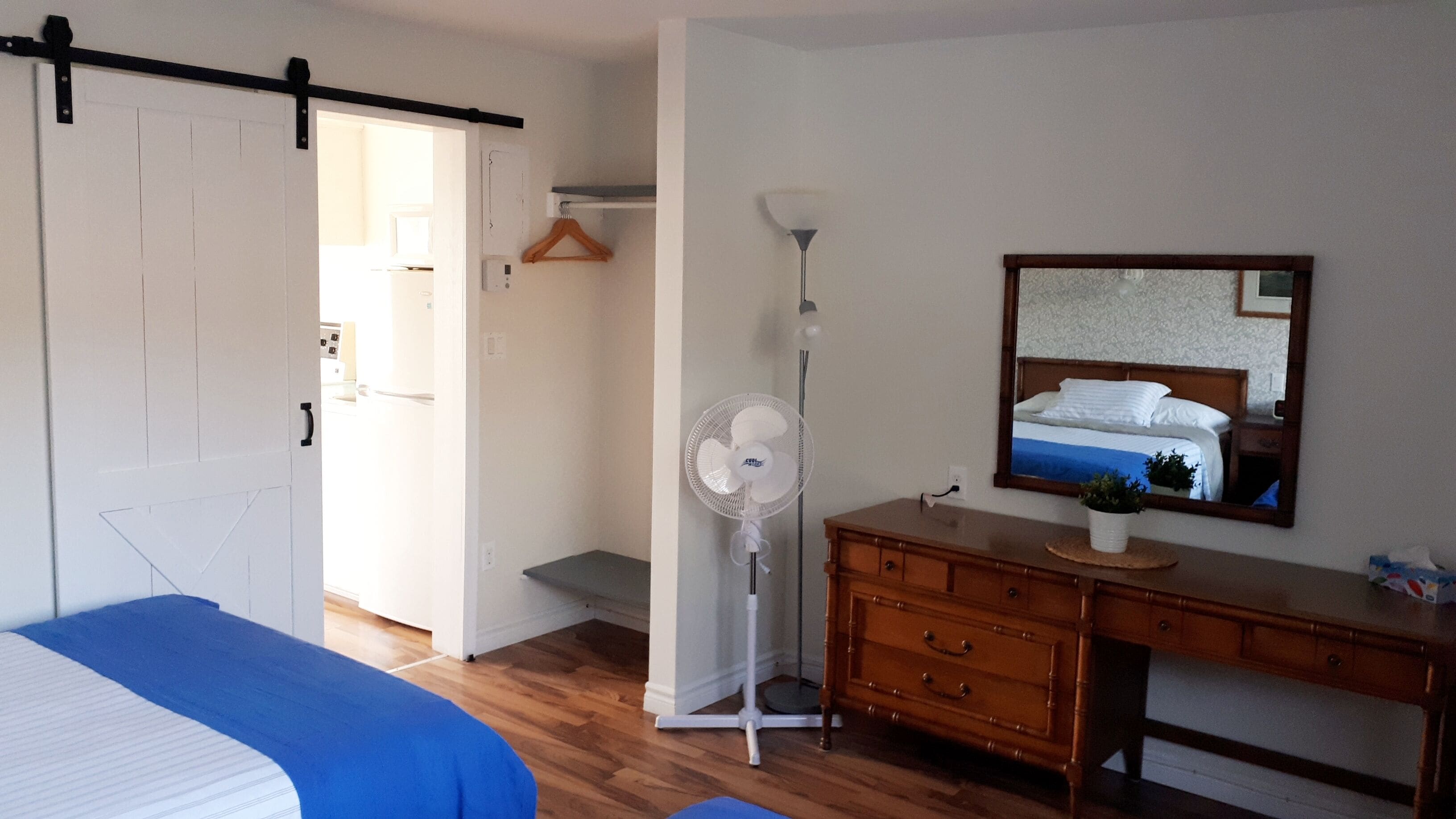 A bedroom with a bed, dresser, mirror, and a standing fan.