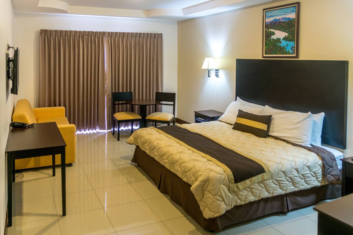 A hotel room with a bed, a desk, a chair, a lamp, and a painting on the wall.