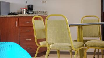 Un comedor con sillas amarillas y una mesa, armarios de madera y una cafetera sobre la encimera.