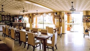 A spacious dining area with high ceilings and ornate ceiling patterns, featuring multiple dining tables and chairs.