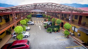 A multi-story hotel with a covered parking area, multiple vehicles, and potted plants.