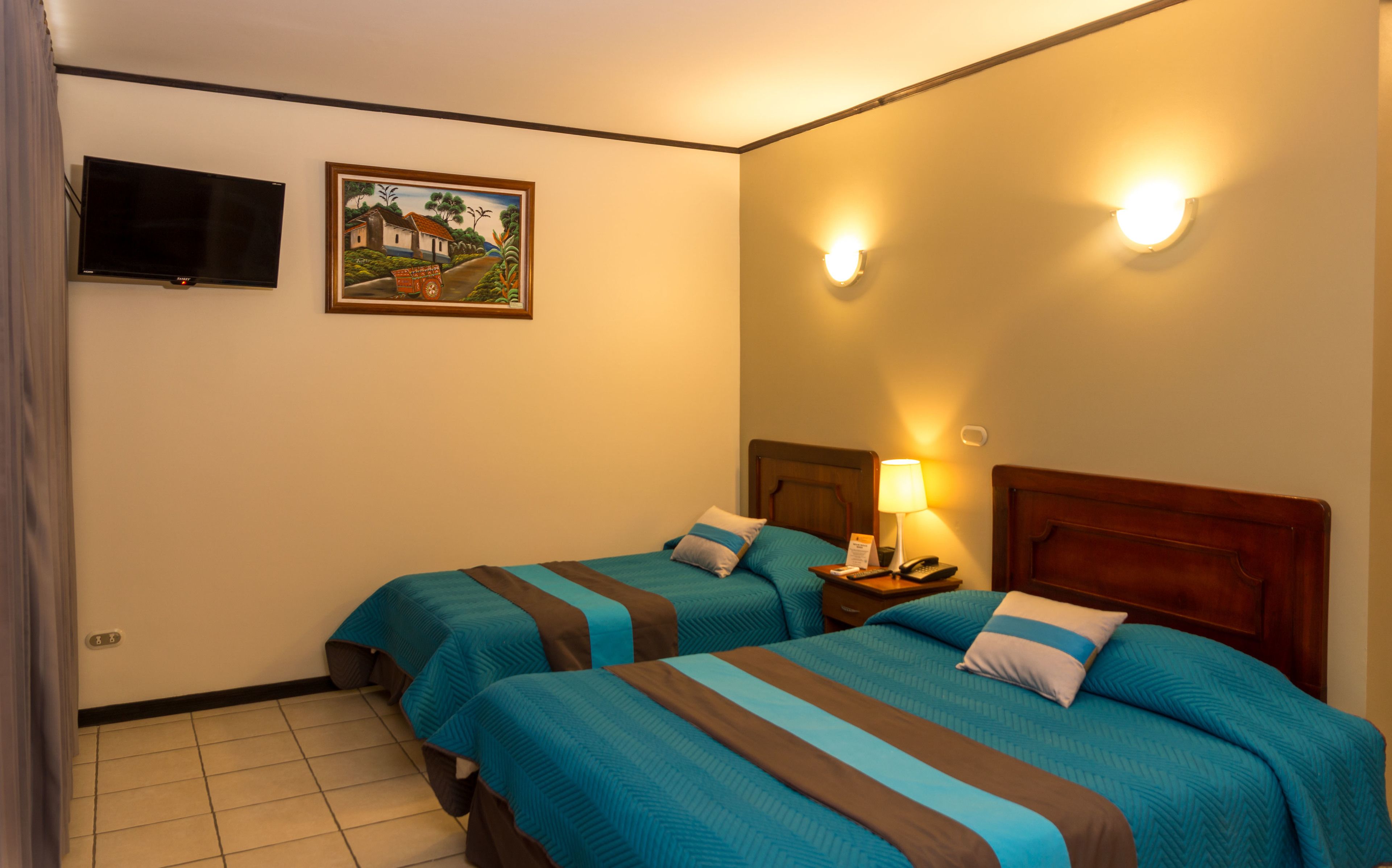 A hotel room with two beds, a flat-screen TV, a painting, and a nightstand with a lamp.