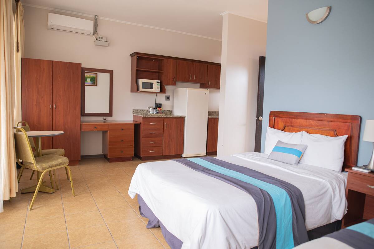A hotel room with a bed, a desk, a chair, a microwave, and a refrigerator.